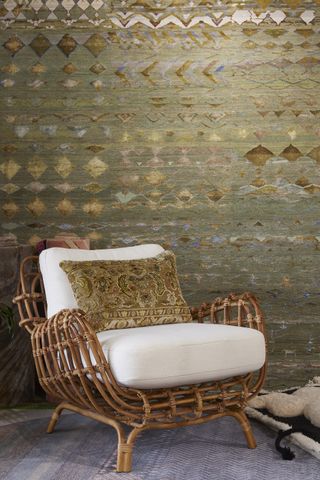 A beautifully crafted armchair in shearling and bamboo sits atop a light blue rug and in front of a geometrically decorated tapestry in tones of green, blue, brown, and yellow.