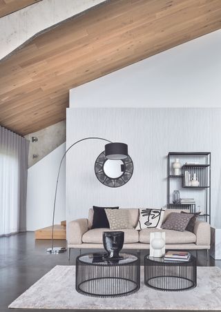 white living room with grey floor, modern coffee tables and matching shelving unit, black floor lamp, black mirror, cream sofa