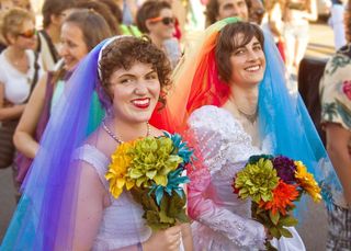 Same-sex female couple in wedding gowns with rainbow colored vails