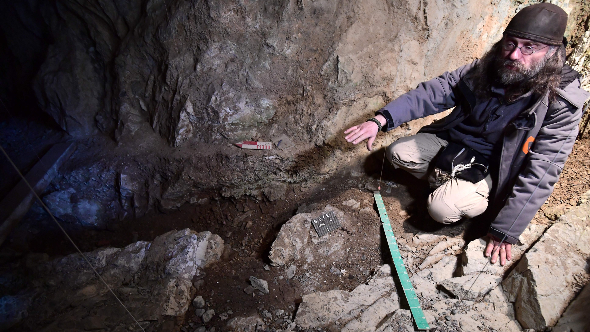 a man in a cave points to an area that has been excavated