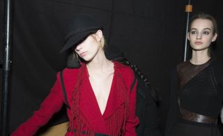 2 Female models dressed in the Lanvin A/W 2015 backstage of the fashion show. Model on the left is in a red outfit and black hat and model on the right is in a black dress
