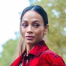 Zoe Saldana wearing a red plaid coat, plaid button down, velvet green skirt, and black leather knee-high boots