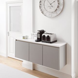 Set of sleek grey wall hung units in a white space set up to hold coffee machine, mugs and coffee accessories