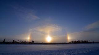 sundogs appear as two bright pillars of light on either side of the shining sun in the winter sky. 