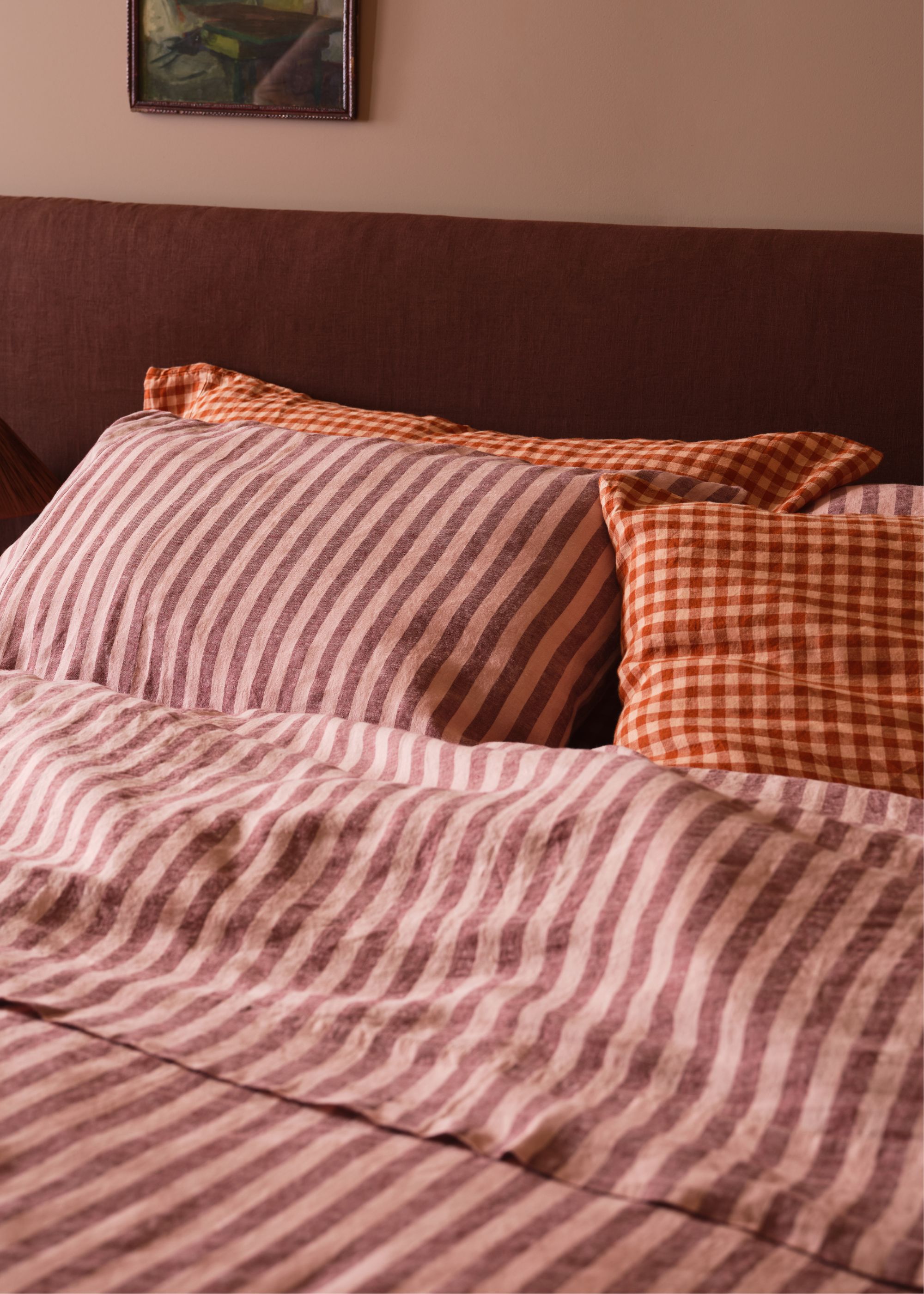 A bed with pink striped bedding and a dark red-brown headboard.