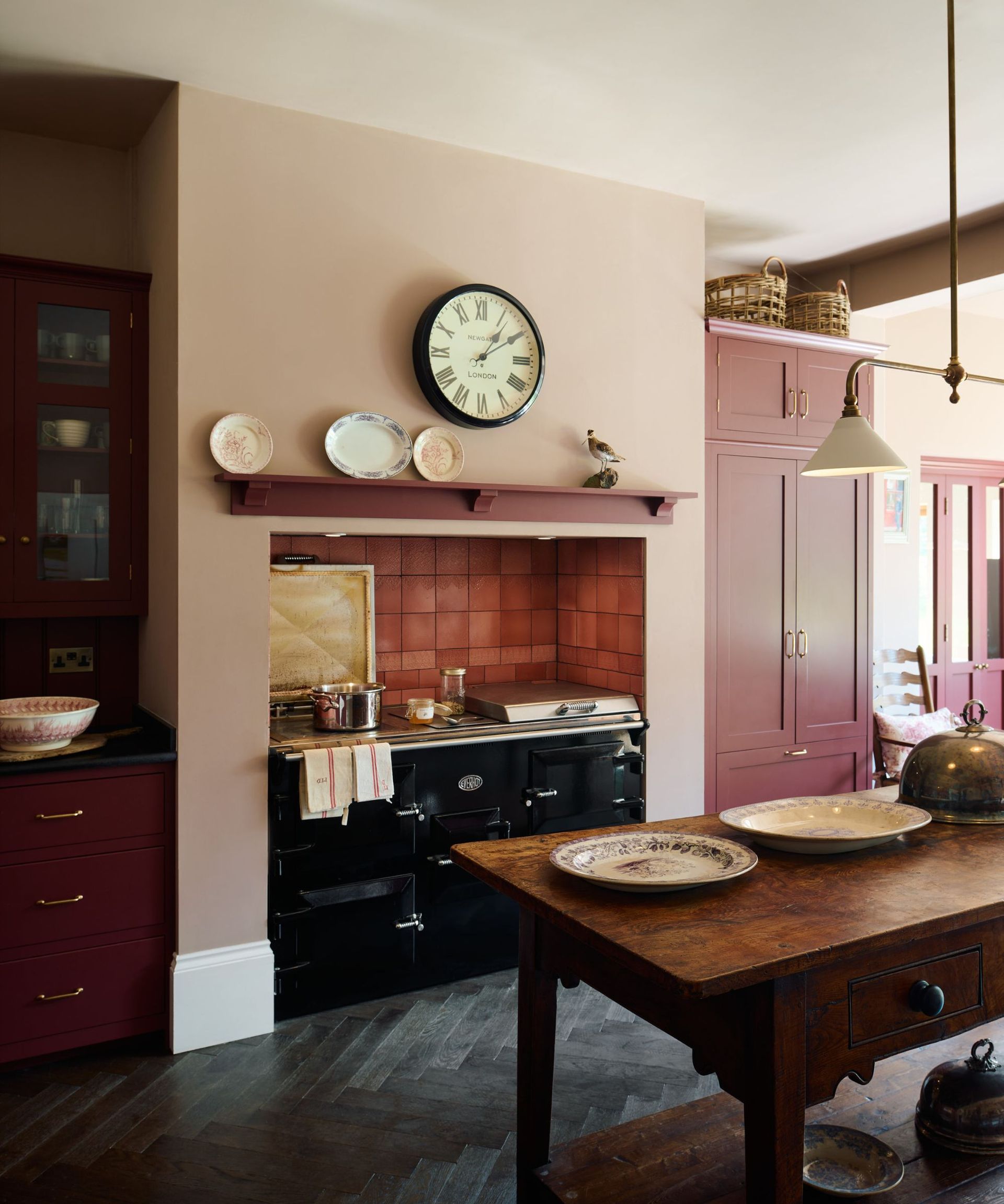 A kitchen with light pink walls, dark pink tiles, a wooden island, and a traditional range cooker inset to an alcove
