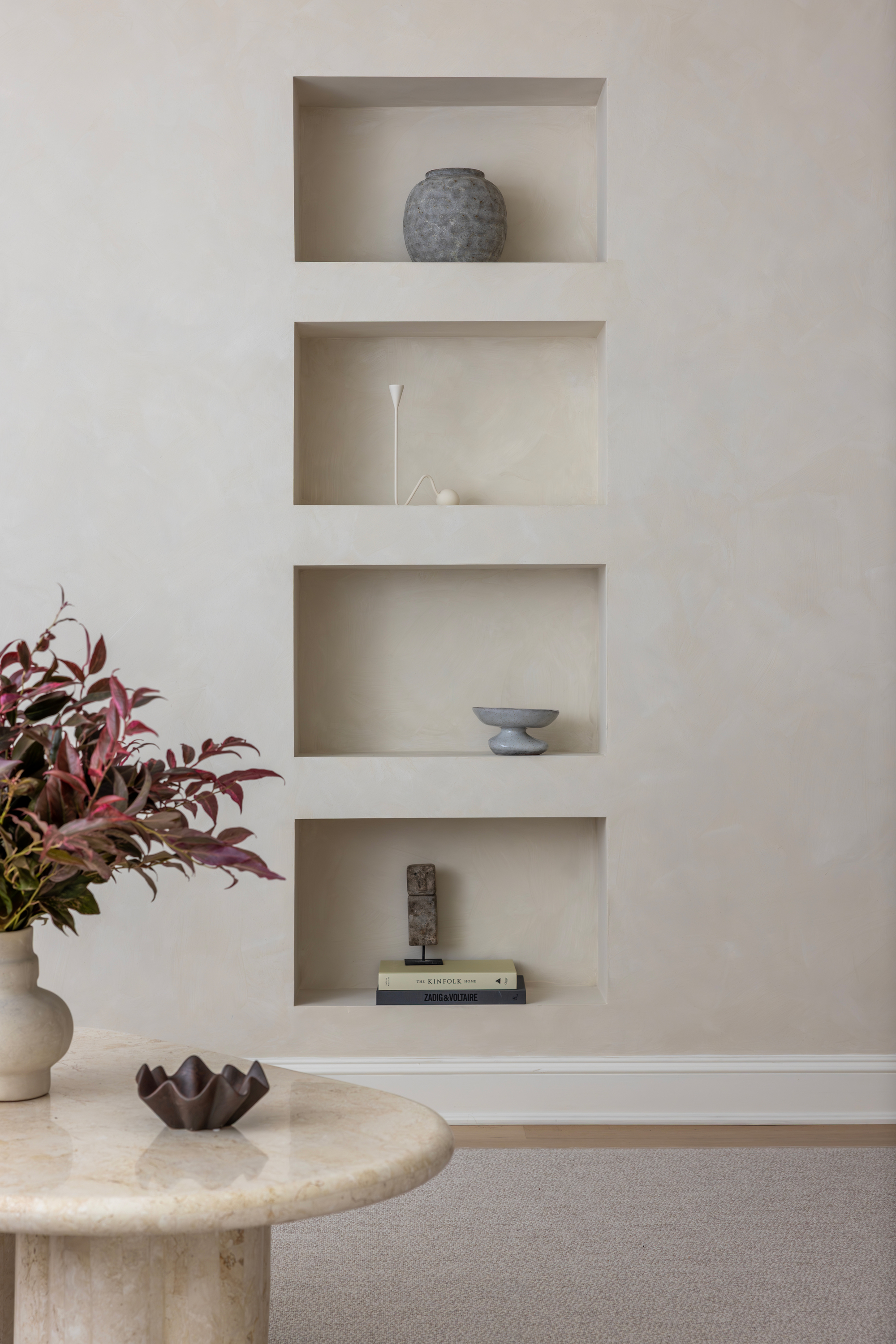 Image of a limewash cream wall with shelving built into the wall. There are muted blue vases and candle holders on the shelves.