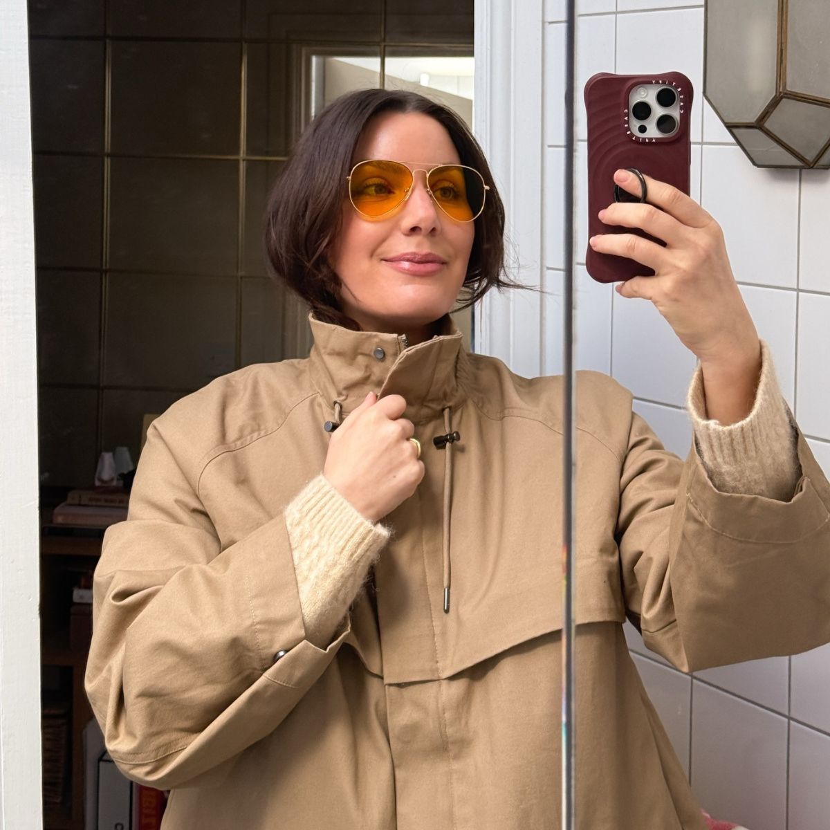 Influencer @emmahoareau taking a mirror selfie wearing a spring jacket and orange-tinted sunglasses