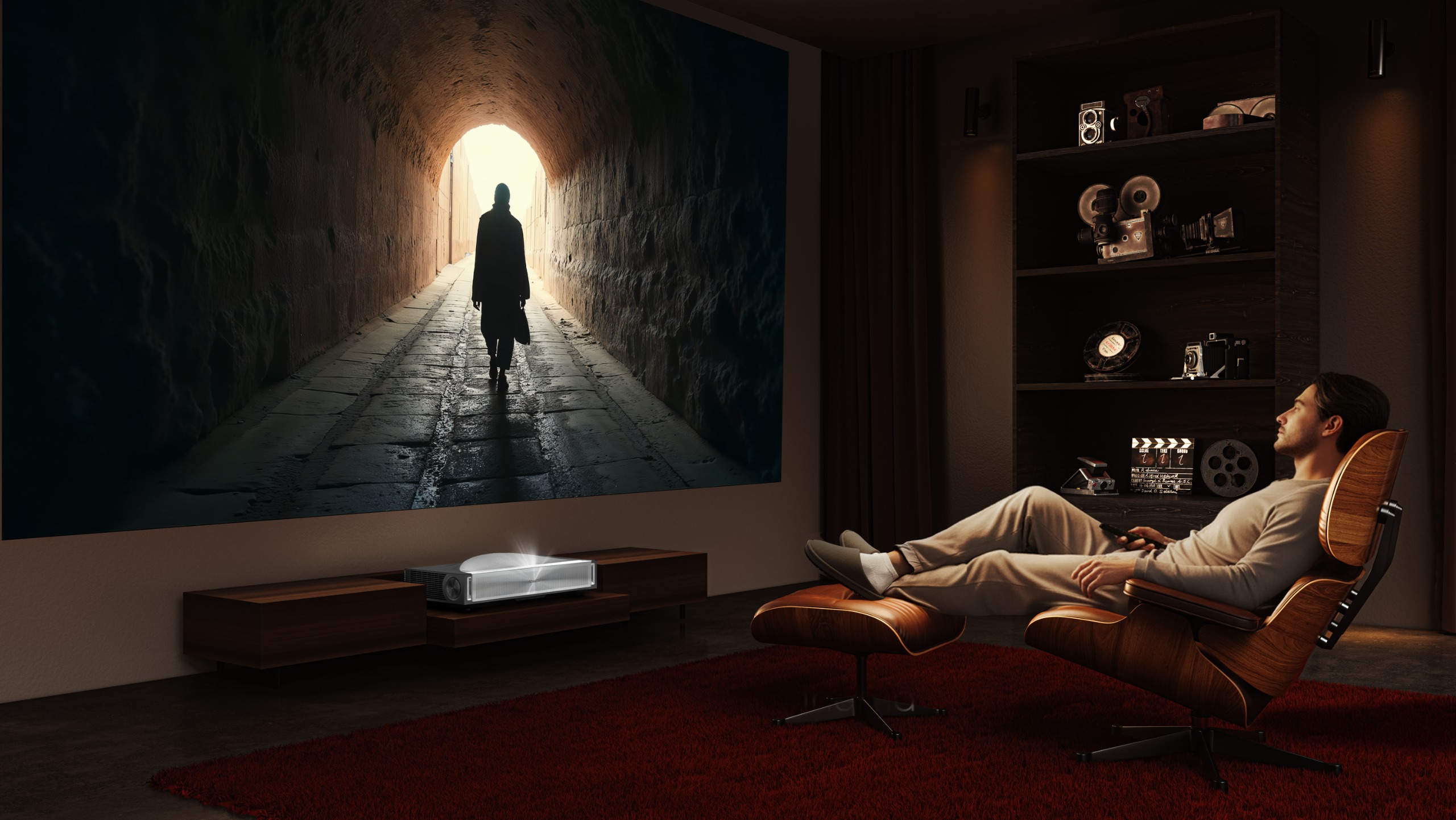 A modern living room with a man reclining in a chair watching a film being projected onto a screen by the PX4-Pro. The film shows a man walking through a tunnel