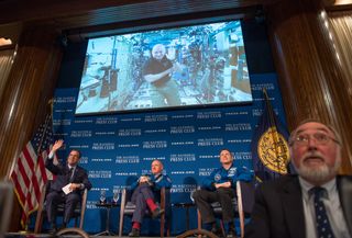 NASA astronaut Scott Kelly on the International Space Station (via video at top) waves while talking with reporters at the National Press Club in Washington, D.C. on Sept. 14, 2015 during a discussion of his one-year space mission. Kelly's identical twin brother Mark Kelly (a former NASA astronaut) sits at center, with National Press Club president John Hughs at left and astronaut Terry Virts at right.