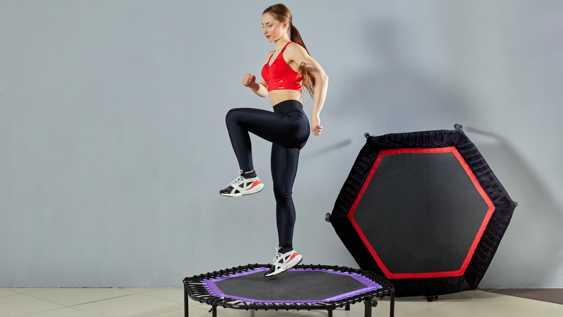 Woman in activewear bouncing on a mini trampoline with one knee raised