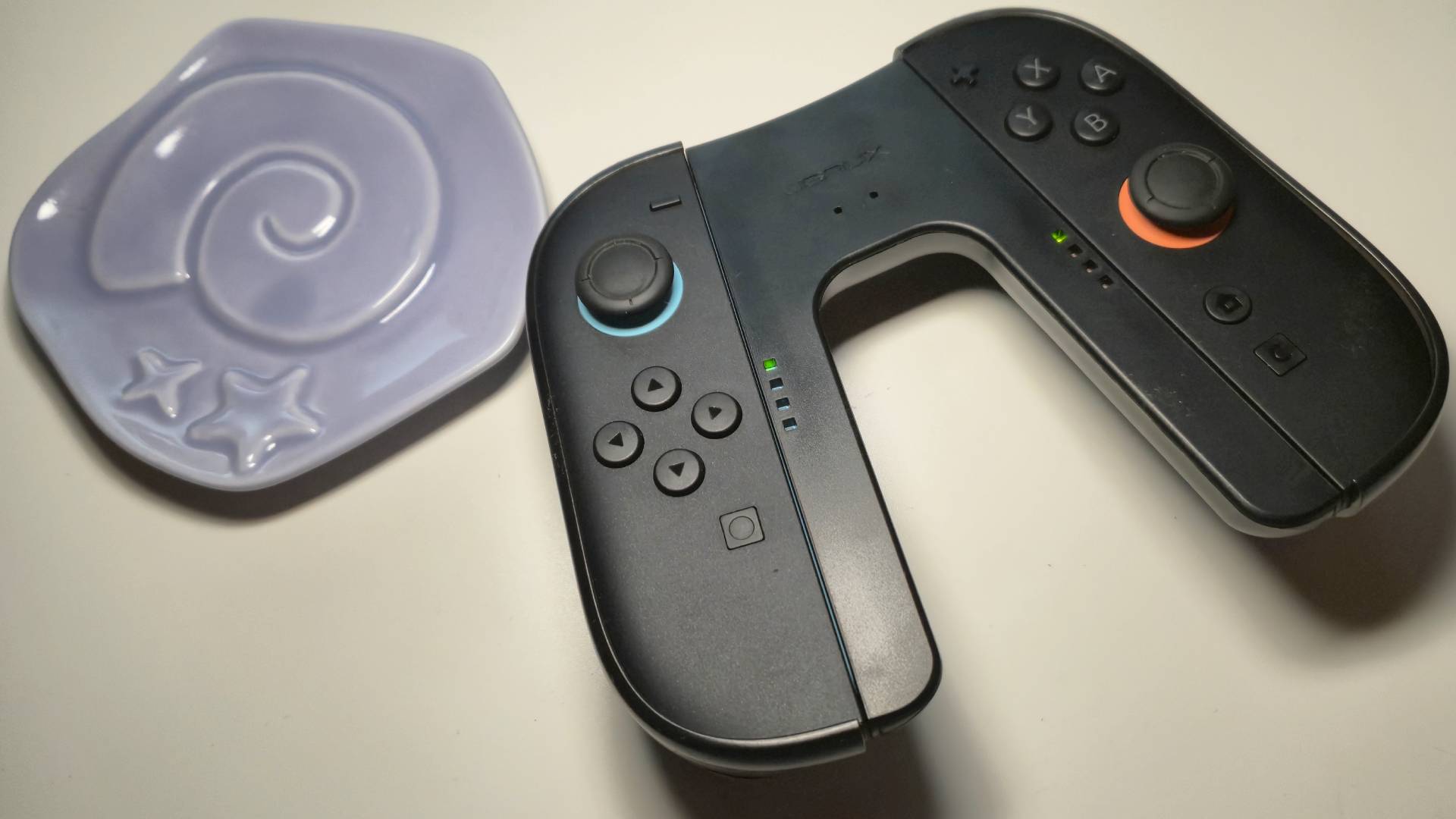 Image of the JSAUX Switch 2 charging grip sitting next an official Animal Crossing plate shaped like a fossil.
