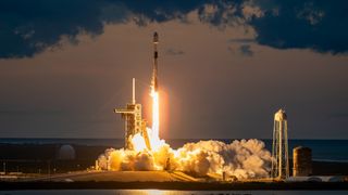 a black-and-white spacex falcon 9 rocket launches into a darkening evening sky.