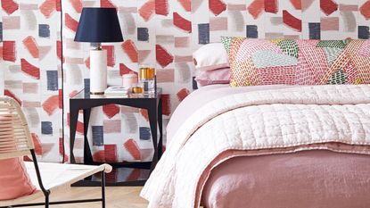 pink bedroom with patterned wallpaper, nightstand and lamp