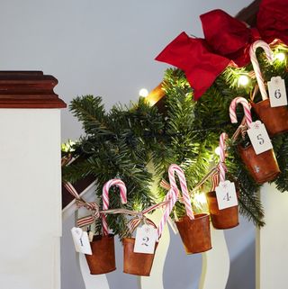 Small copper pails attached to faux green garland and candy sticks hanging on wooden balustrade
