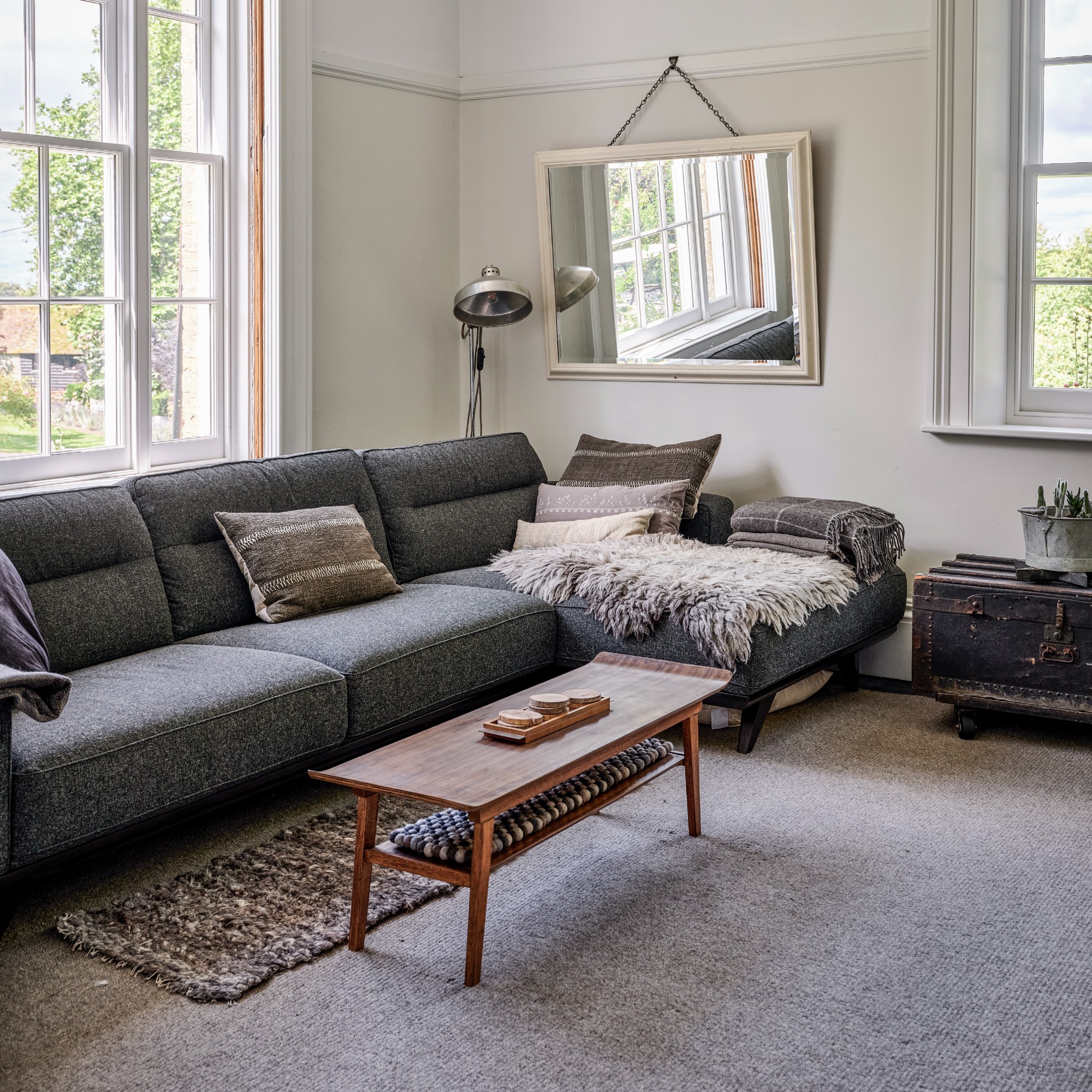 A bright living room with a dark grey chaise sofa and a chrome floor lamp behind it