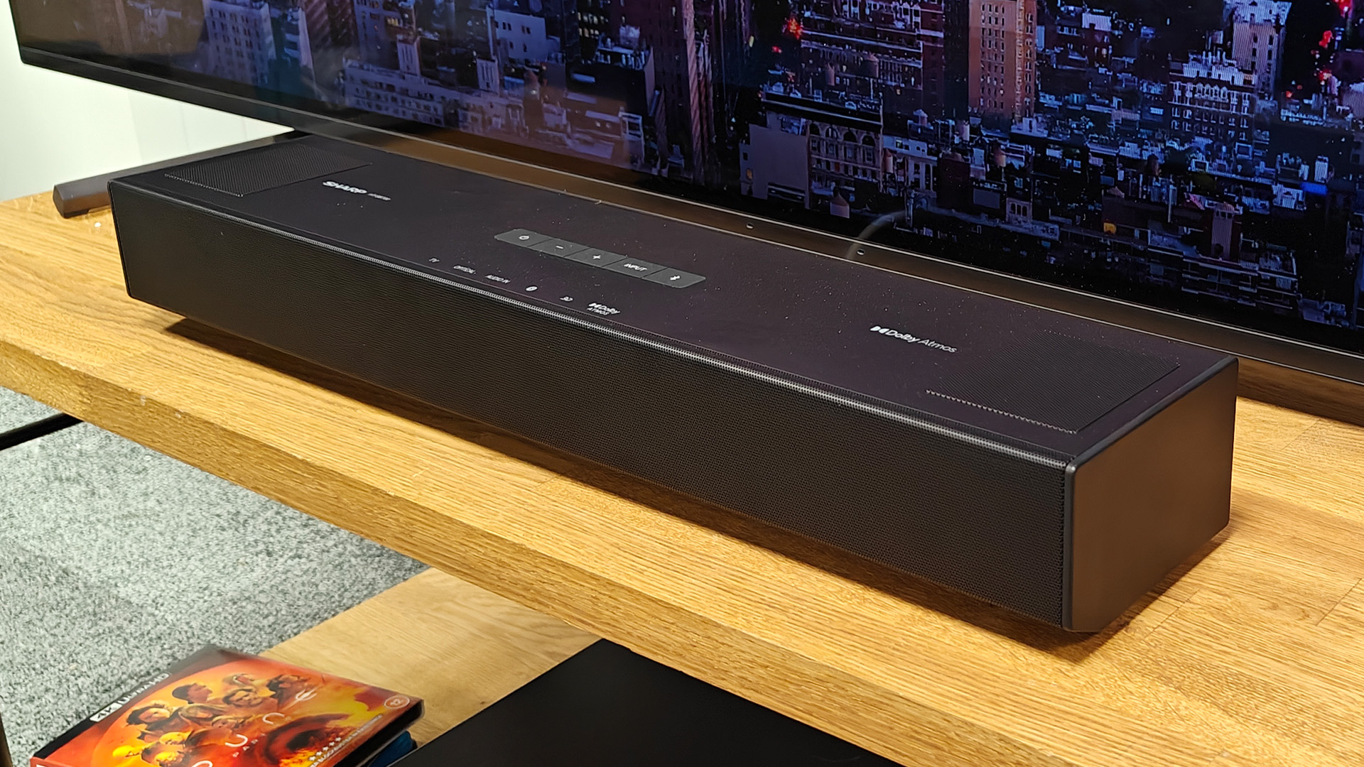 Sharp HT-SB700 Dolby Atmos soundbar on wooden AV rack in front of TV