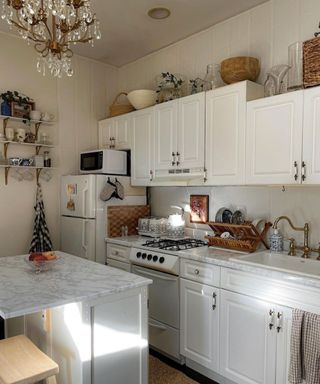 A white small kitchen with cabinets, a countertop, fridge, and a chandelier