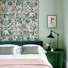 A green bedroom with a floral fabric wall hanging behind the bed