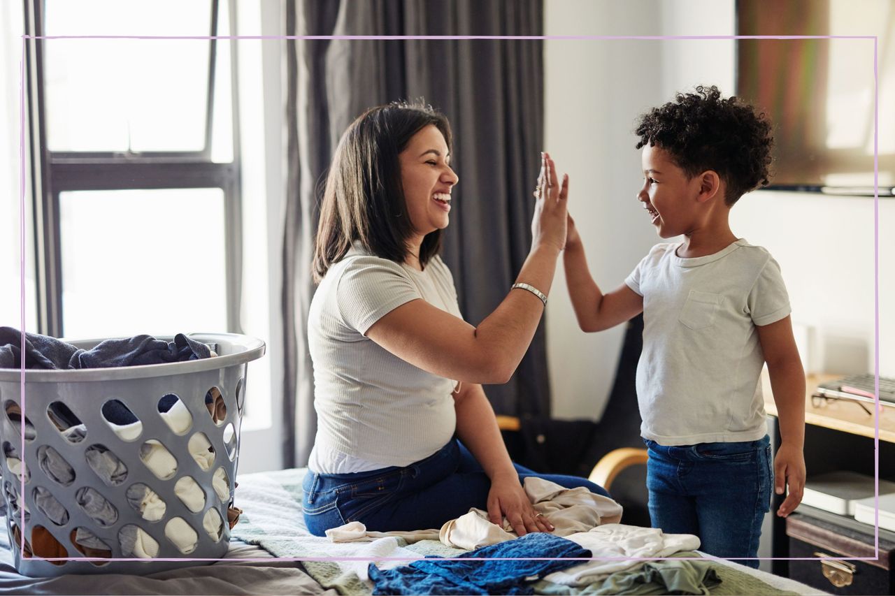 A mum high fiving a young boy while sat next to a pile of washing