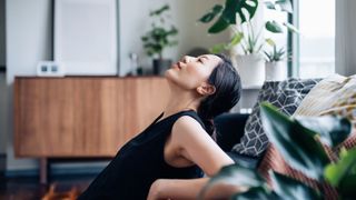 Woman taking a break at home, sitting with head back against the sofa