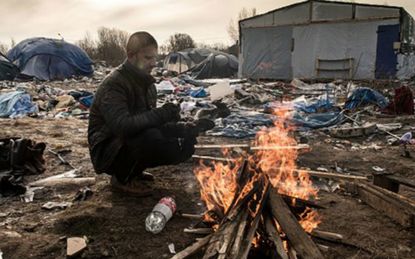 A refugee keeps warm at the Jungle refugee camp in Calais