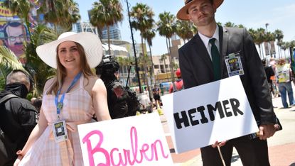 A woman dressed in pink holding barben sign next to a man in a black suit holding heimer sign