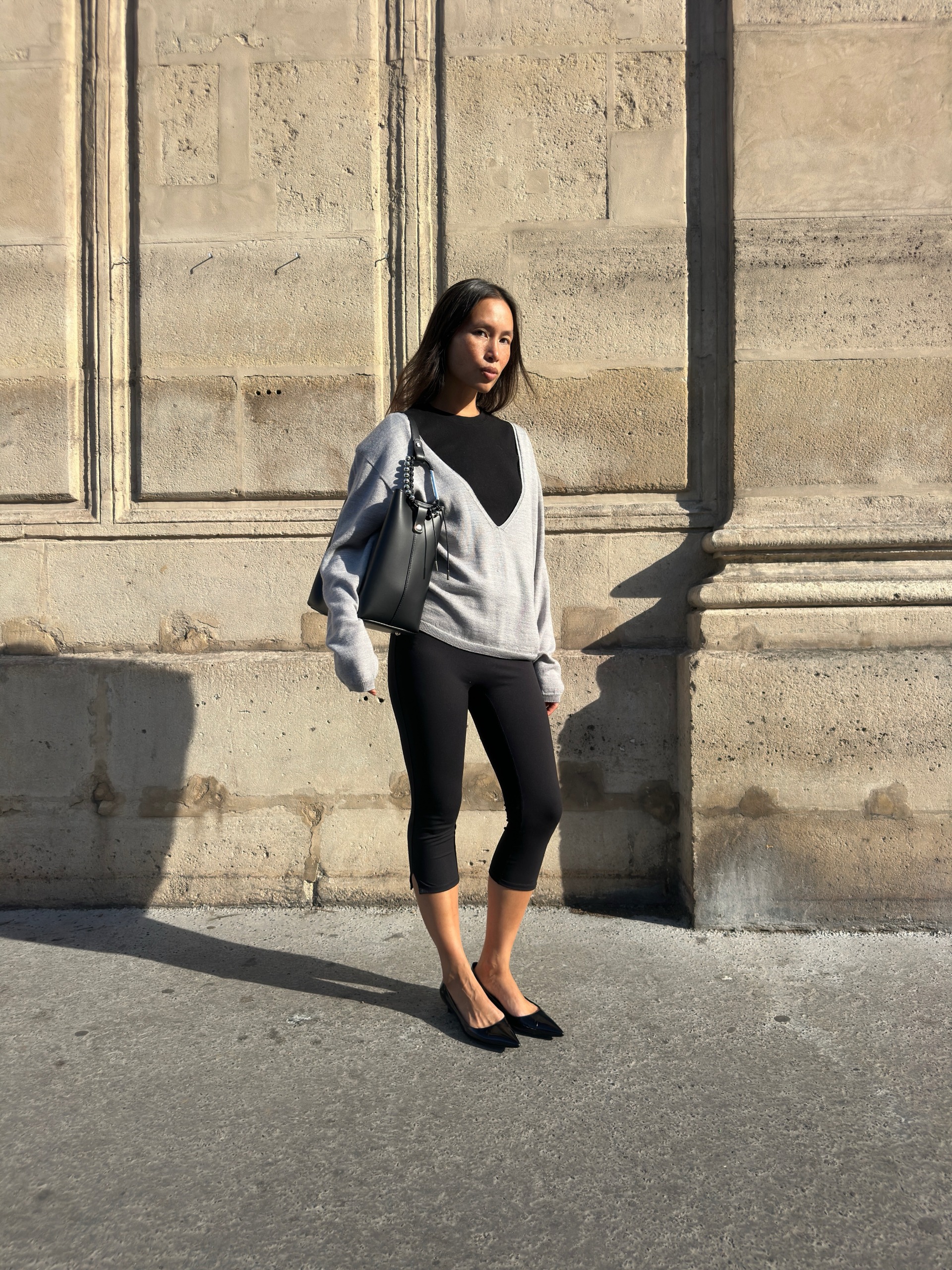 An image of @vikilefevre wearing a black t-shirt, grey v-neck jumper and capri leggings.