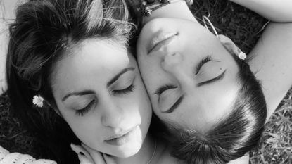 Two women lay on the grass, heads touching.