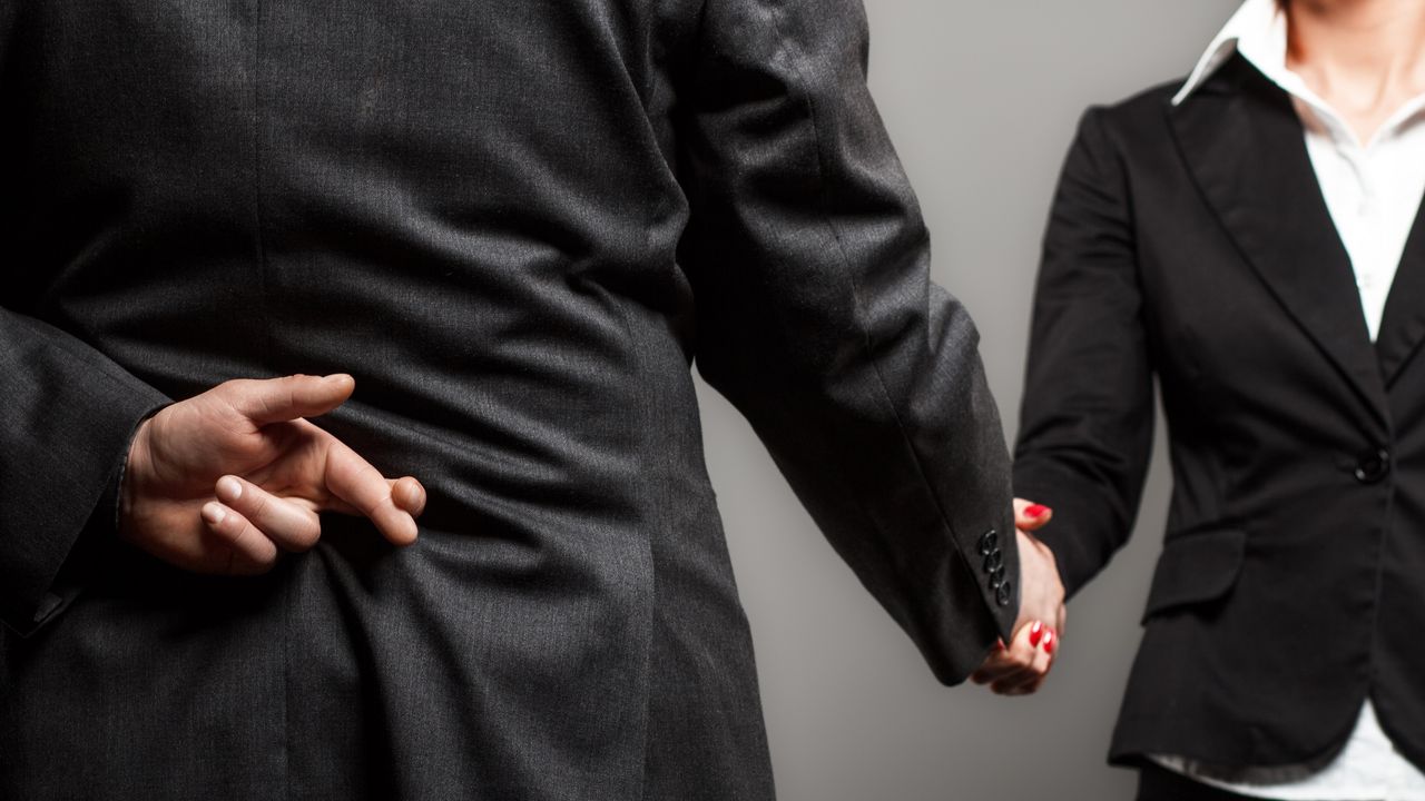 A businessman hides his crossed fingers behind his back as he shakes a woman&#039;s hand.