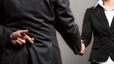 A businessman hides his crossed fingers behind his back as he shakes a woman's hand.