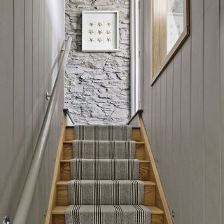 A narrow grey stairway with a striped runner leading to a textured grey wall