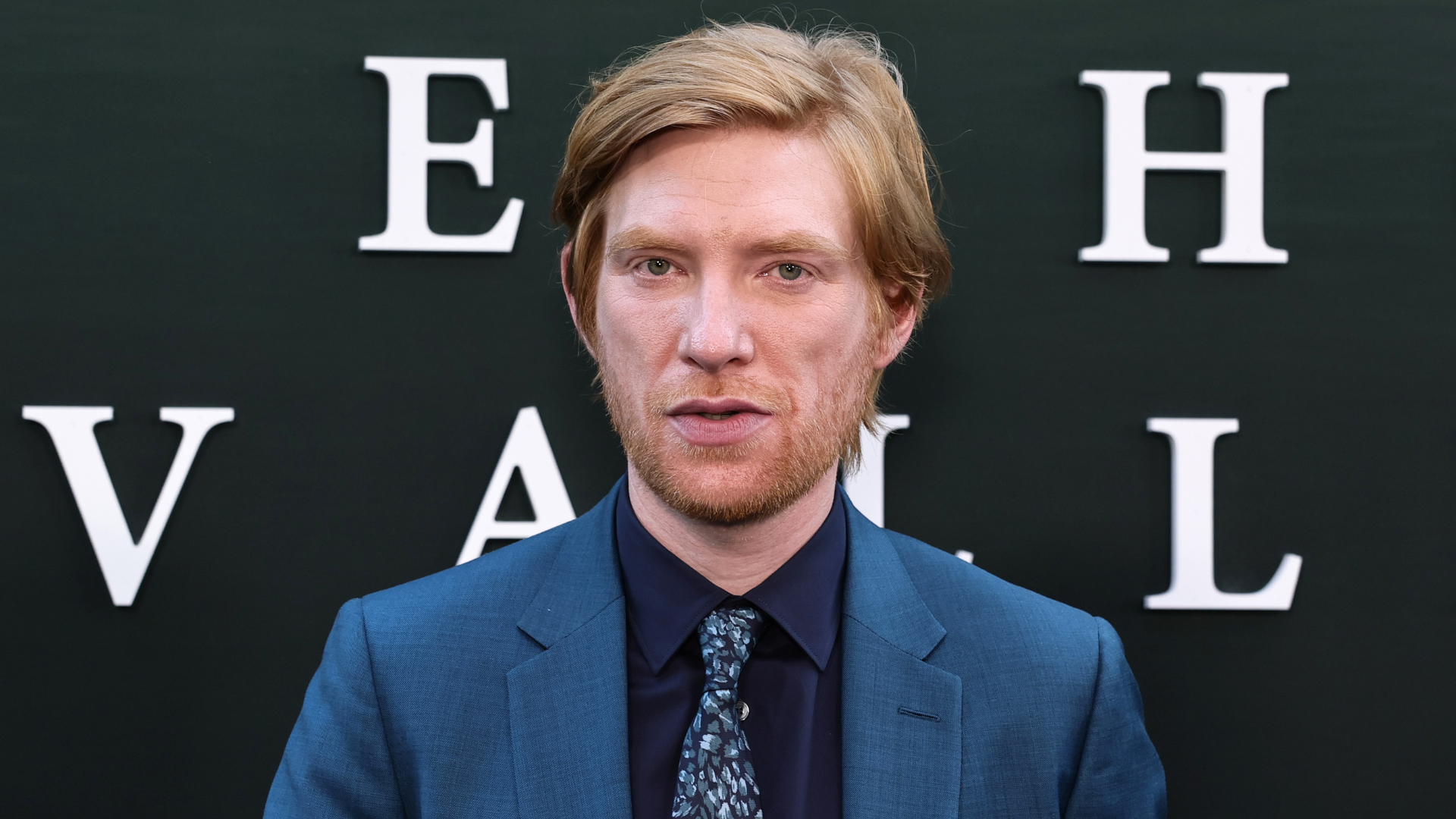 Domhnall Gleeson attends the "Echo Valley" New York Premiere at AMC Lincoln Square 13 on June 04, 2025 in New York City. He is wearing a blue suit with a dark blue shirt and blue patterned tie. He is standing in front of the backdrop for Echo Valley