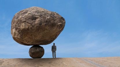 An illustration shows a large rock precariously balanced atop a small one, looming over a person standing underneath.
