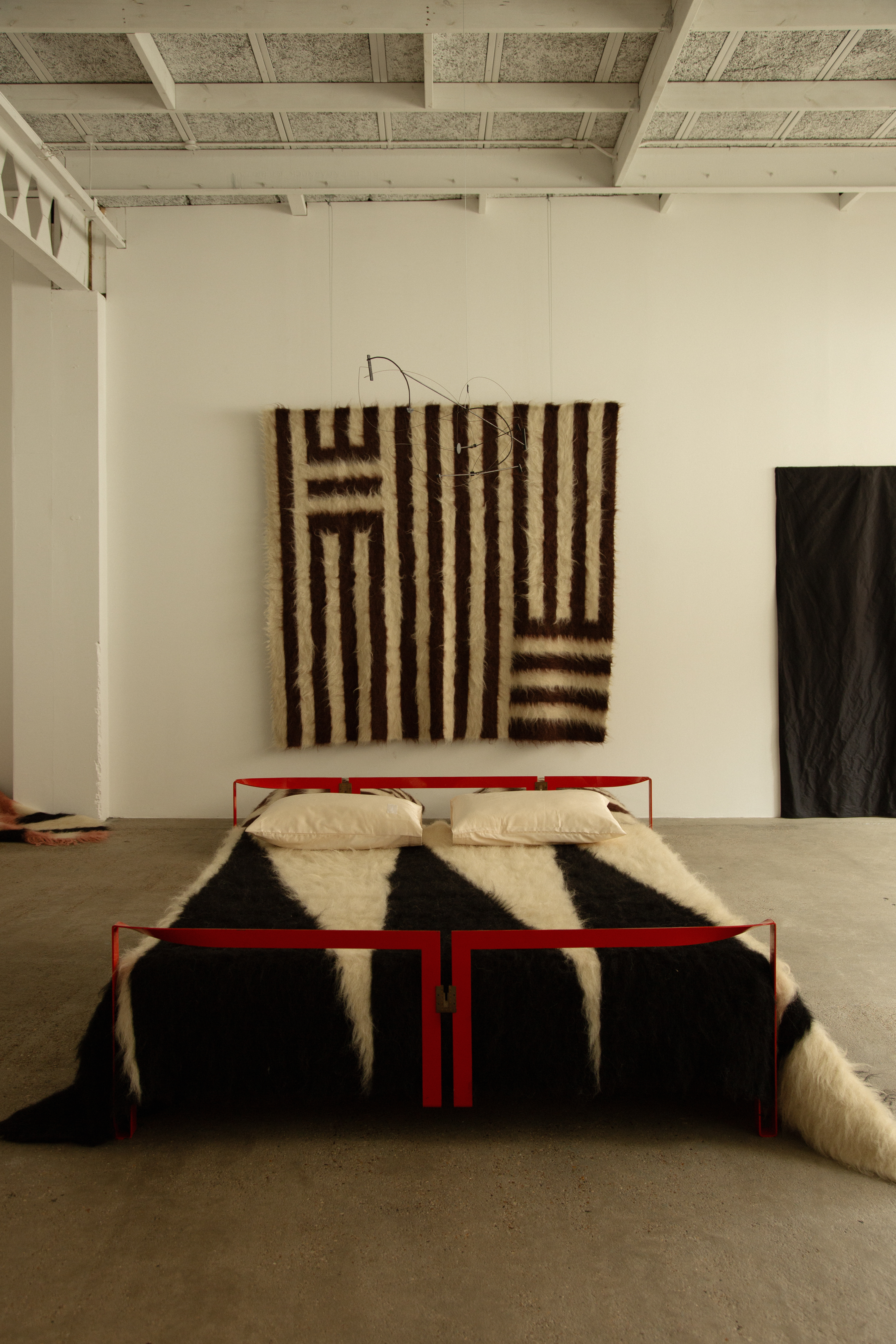 A series of textile creations with an abstract, textural wool feel sit in an industrial showroom alongside iconic modernist designs.