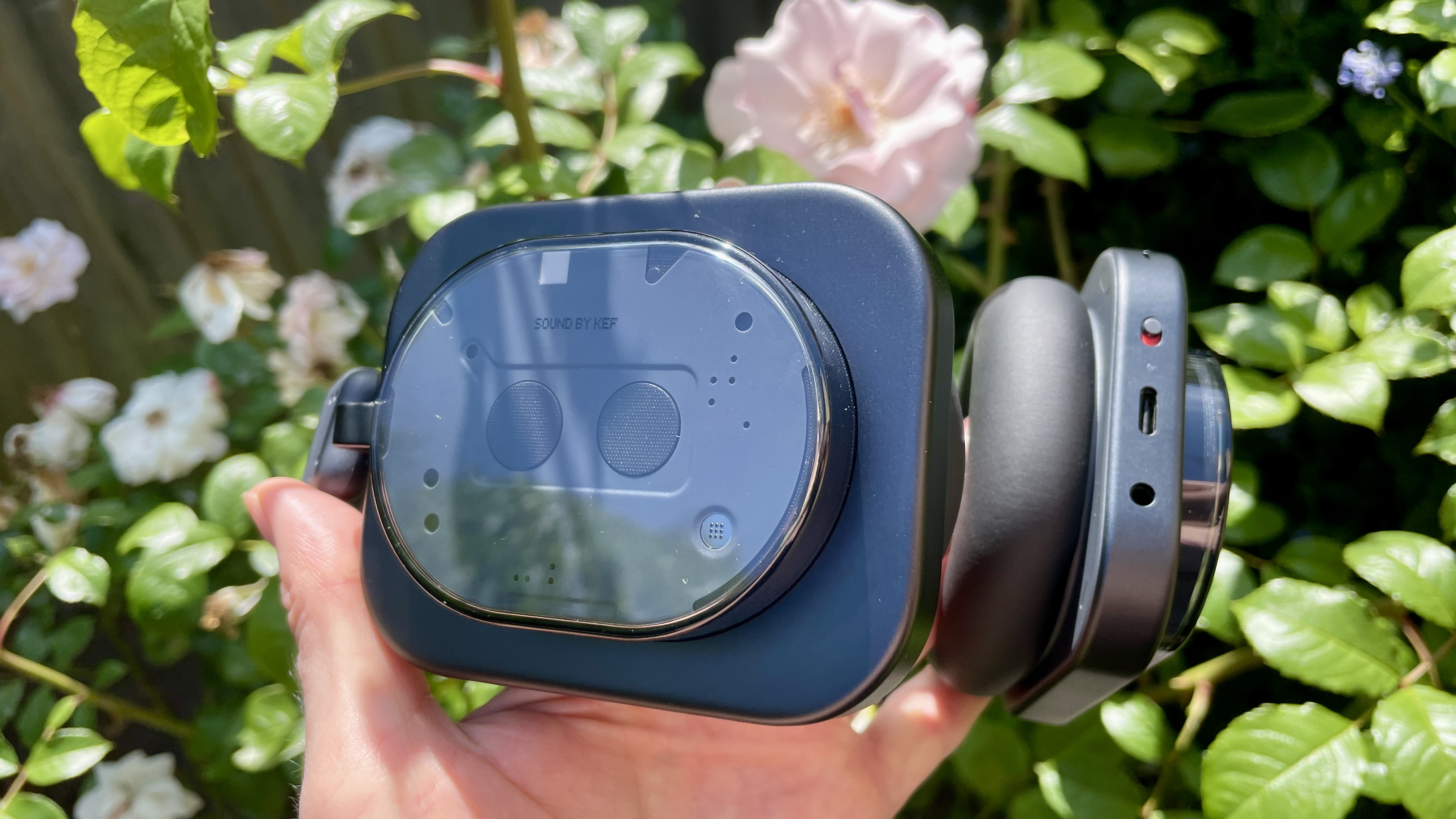Nothing Headphone (1) in black, on a pink rose and floral background, held in a woman&#039;s hand