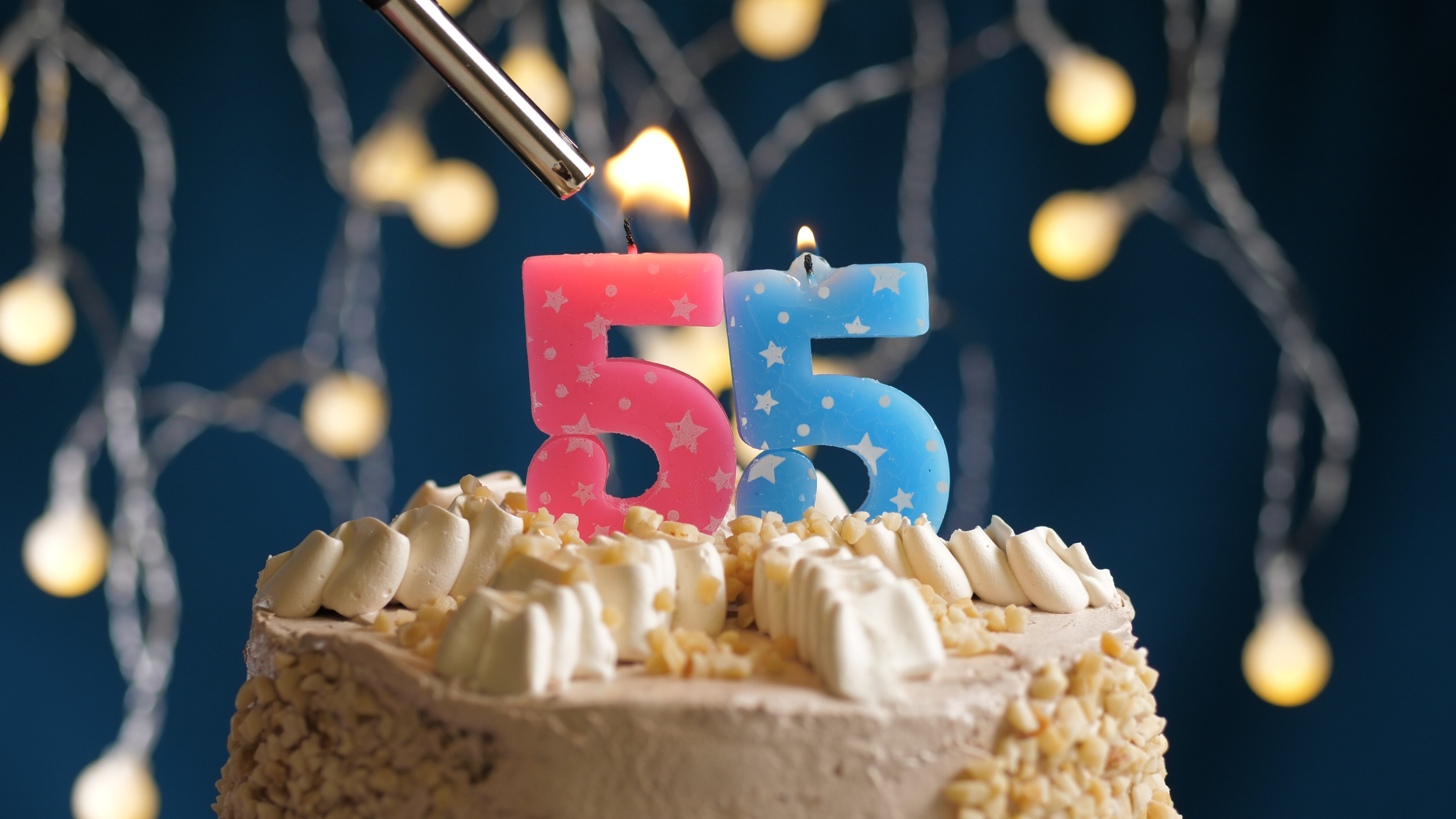 Birthday cake with 55 number candle on blue backgraund set on fire by lighter. Close-up view candles