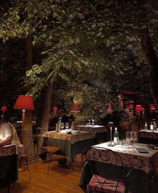 Outdoor dining area of Al Garghet Milan restaurant with tartan tablecloths and a canopy of trees