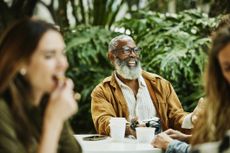 Medium shot of smiling senior man relaxing at outdoor café during vacation in city. He holds a camera.