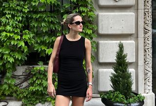 Eliza Huber wearing a black Norma Kamali minidress with black mules, a burgundy bag, sunglasses, and a slicked back bun.