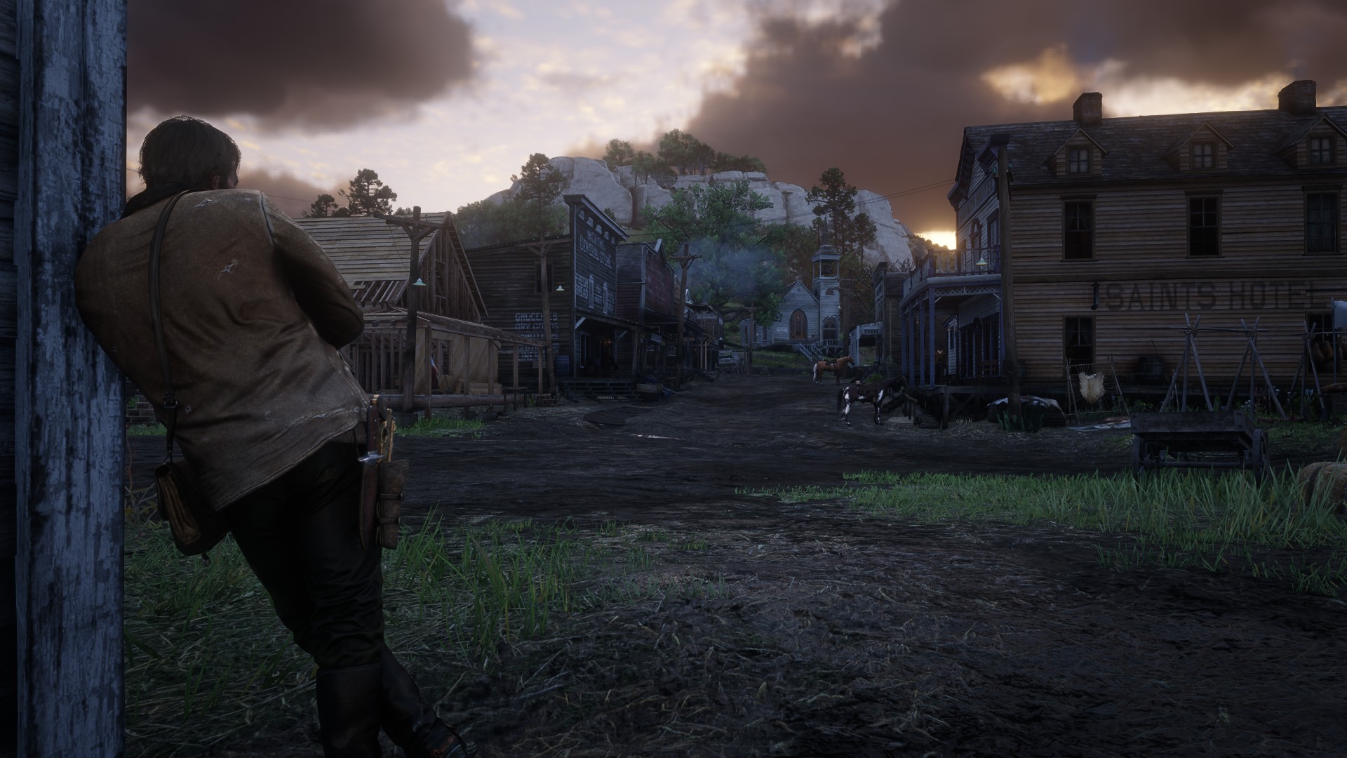 Arthur leaning against a house in a town during sunrise in Red Dead Redemption 2