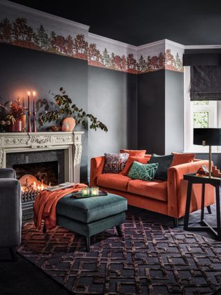 gray and orange living room with emerald green footstool, orange sofa, ornate fireplace, candles, foliage and vases on mantel, fall freeze, textured rug