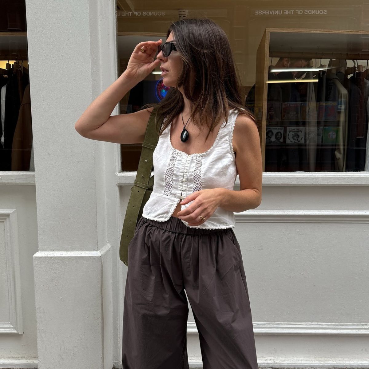 Woman wears white blouse, brown trousers, green suede bag