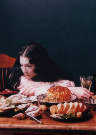 michelle zauner of japanese breakfast lays her head on her arm at a table with lots of food