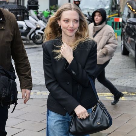 Amanda Seyfried walks outside in London wearing two-tone jeans with a black collarless blazer and black pointed-toe shoes.