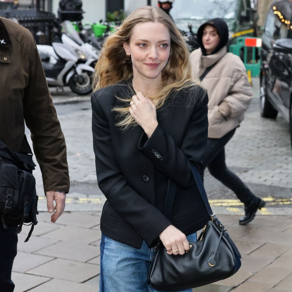 Amanda Seyfried walks outside in London wearing two-tone jeans with a black collarless blazer and black pointed-toe shoes.