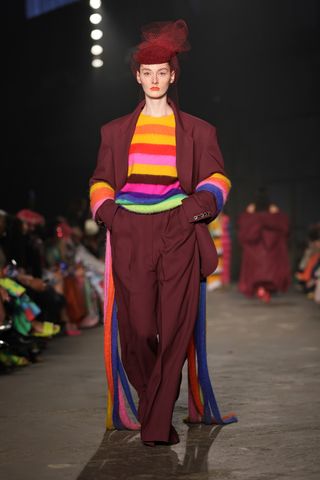 A model walks the runway for the Christopher John Rogers Collection 010 runway show at Brooklyn Navy Yard on June 07, 2022 in Brooklyn, New York wearing a rainbow striped sweater and maroon suit