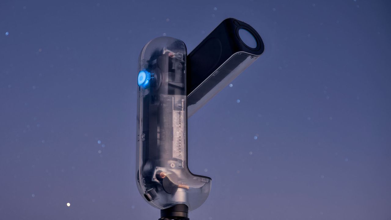A close-up of the Vaonis Vespera II - X edition showing the clear outer shell and inner workings while pointing at the sky with a starry night sky in the background.
