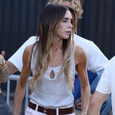 Victoria Beckham wears white straight-leg jeans with a cream vest top and brown leather belt.
