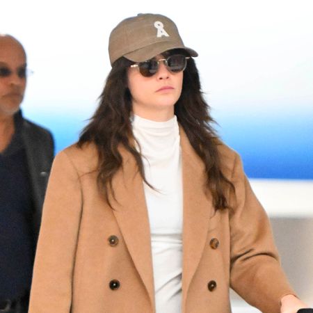 Cara Delevingne wearing cobalt blue pants with a camel coat, cream turtleneck and black suede mules at JFK airport